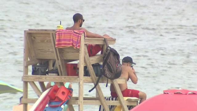 Two lifeguards sit on a lifeguard stand, keeping an eye on the ocean. 