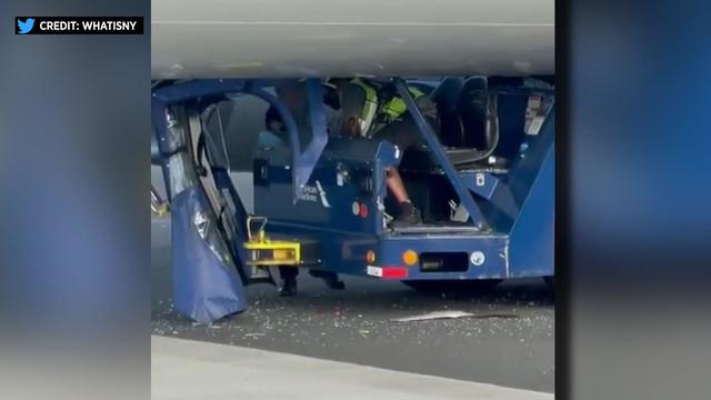 An airplane tug and the driver are pinned underneath an airplane. 