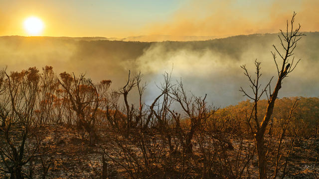 Sun setting in smoldering mountain landscape with smoke-filled valley after forest fire 