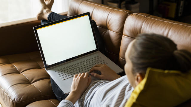 Young woman lying on couch at home using laptop 