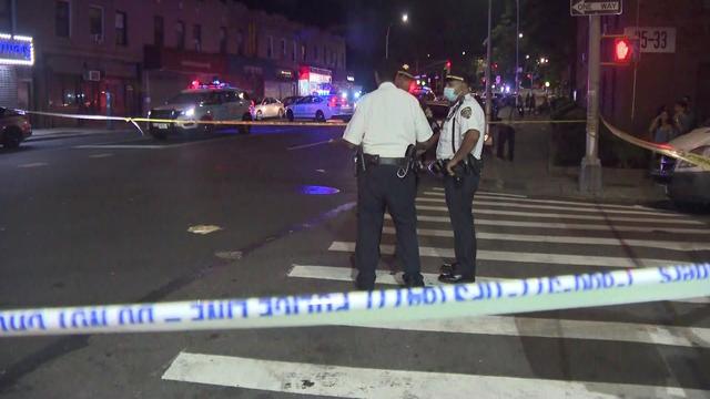Police officers stand in a crosswalk behind crime scene tape. 