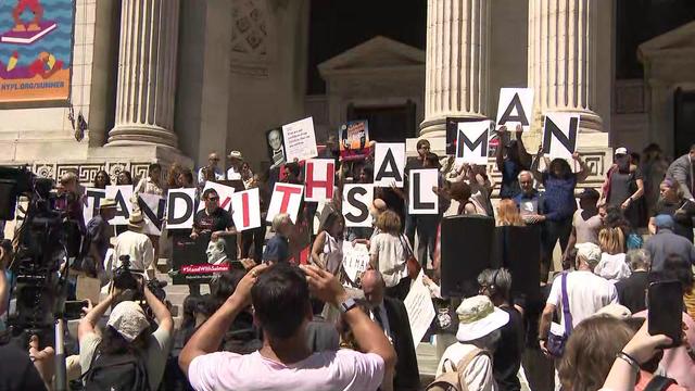 A crowd stands on the steps of the main branch of the New York Public Library, holding signs showing their support for Salman Rushdie. 