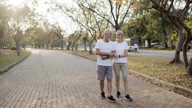 Senior citizen couple taking a walking in a park during summer morning. Seniors couple spend time in public park together 