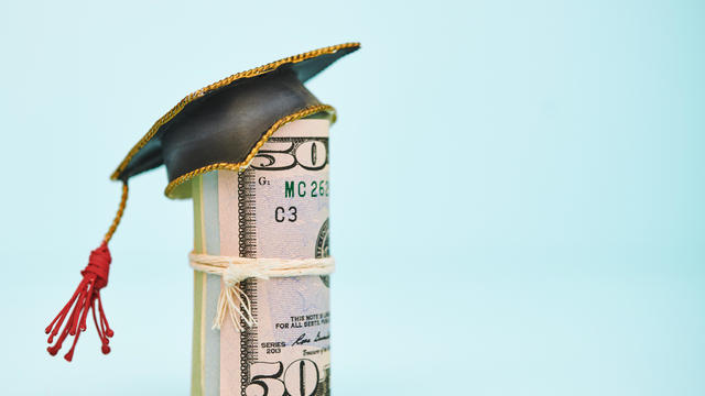 Cost of Education. Money roll wearing a mortarboard graduation cap 