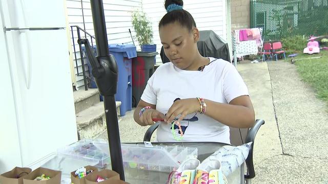 A teenager girl sits at an outdoor patio table, working on arts and crafts. 