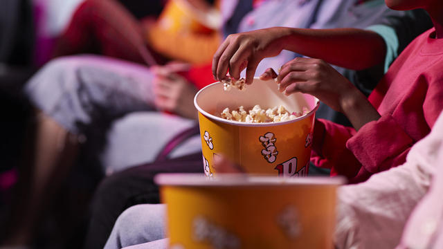 Midsection of friends sharing popcorn while sitting in theater 