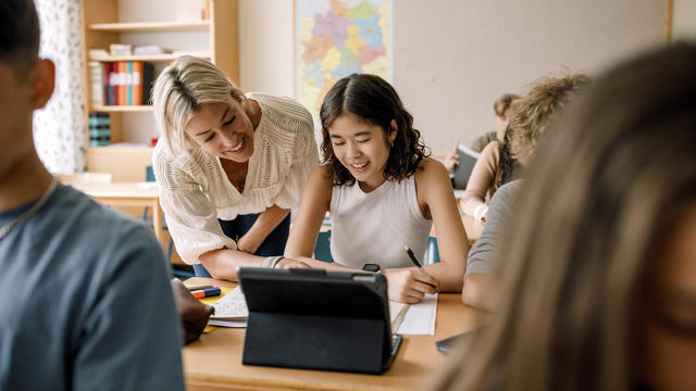 Smiling teacher teaching girl studying on digital tablet in classroom 