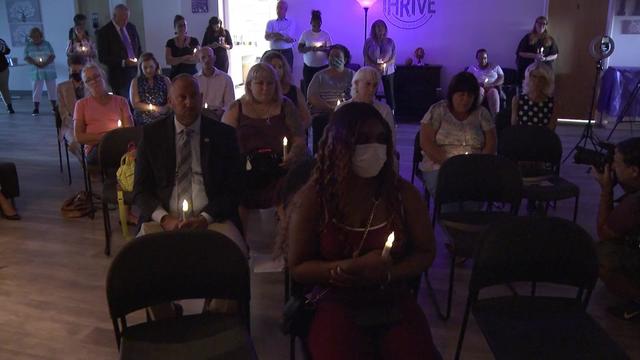 People sit and stand in a dark room, holding plastic candle lights. 