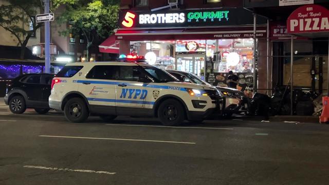 An NYPD vehicle sits parked on the street in front of a corner market. 