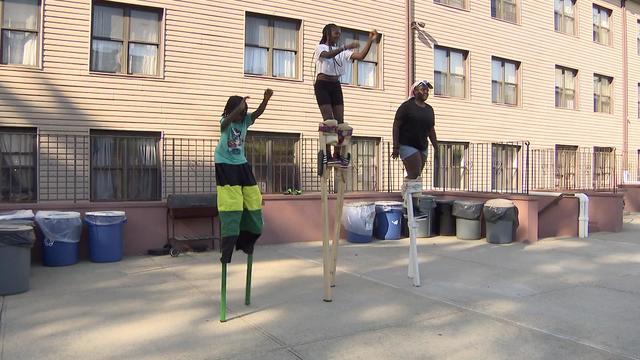 Three young people dance on stilts. 