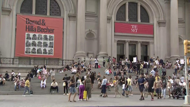 Dozens of people sit on the stairs leading up to the entrance of the Metropolitan Museum of Art. 