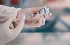 A young doctor in white protective glove is holding a medical syringe and vial 