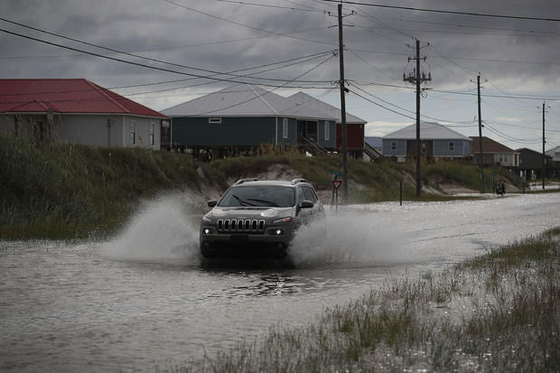 SUV driving along flooded street with houses on the left 