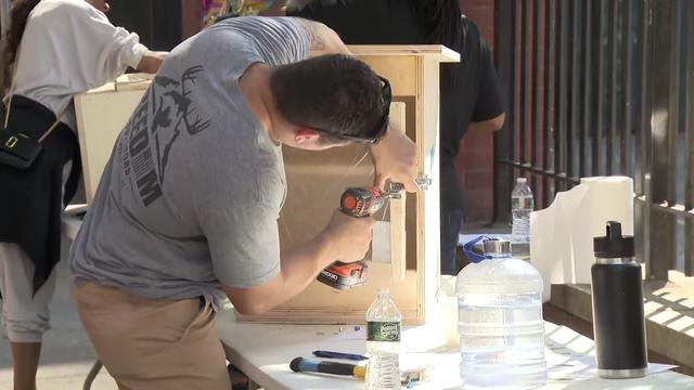 A man uses a drill to build a mini-library. 