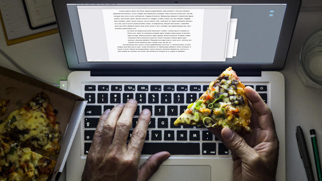 Hand holding a pizza while working on a laptop 