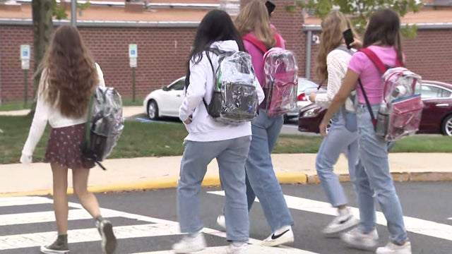 Students carrying see-through backpacks head to school.