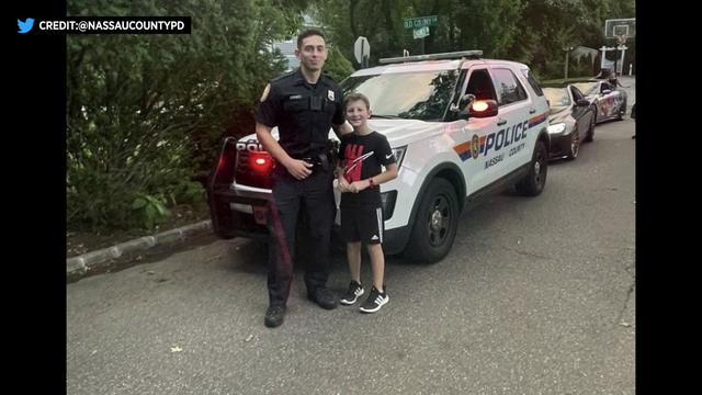 Nine-year-old Mason stands next to a Nassau County police officer in front of a Nassau County Police vehicle. 