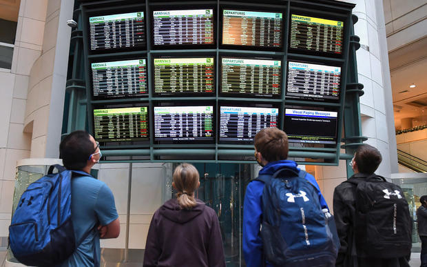 Travelers look at a display board showing cancelled flights at Orlando International Airport 