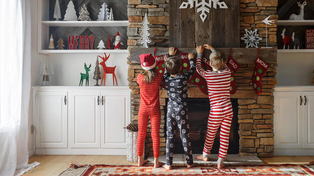 Three children hanging up Christmas stockings on a fireplace 