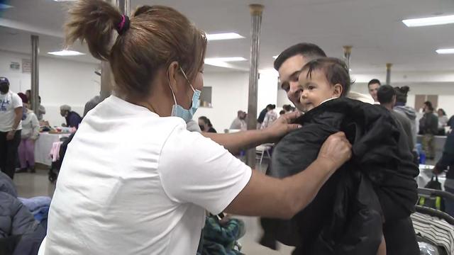 A volunteer helps put a winter coat on a toddler being held by a man. 