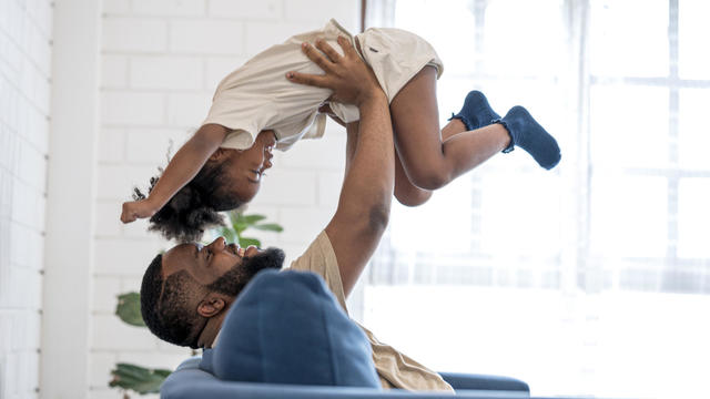 African father picking up daughter in the air, face to face. They are having fun in weekend at home. 