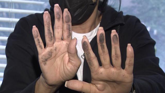 A woman holds up her soot-covered hands after rubbing them on her windowsill. 