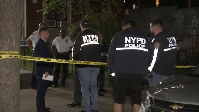 Several NYPD officers stand in front of an behind crime scene tape. 