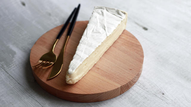 Piece of brie cheese on wooden tray with fork and knife 
