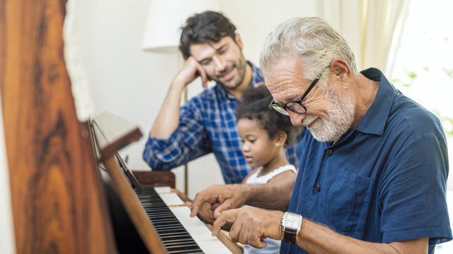 Family spend time happy together. Grandfather playing piano with his granddaughter and son together in living room at home. 