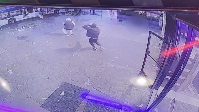 Surveillance video shows two men running outside a Harlem smoke shop during a shooting. 