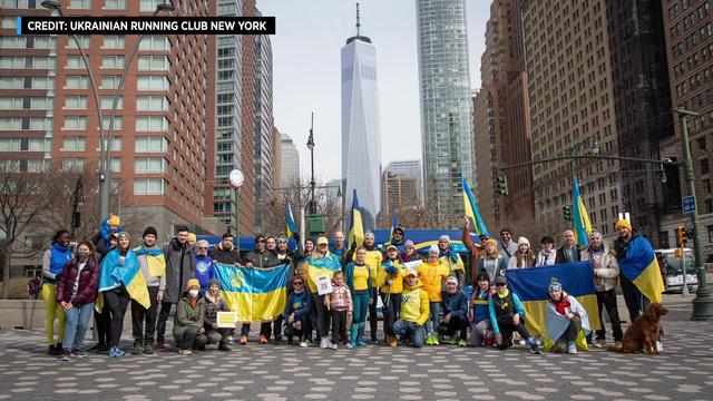 A group of people pose for a photo in New York City, some holding Ukrainian flags or wearing Ukrainian colors. 