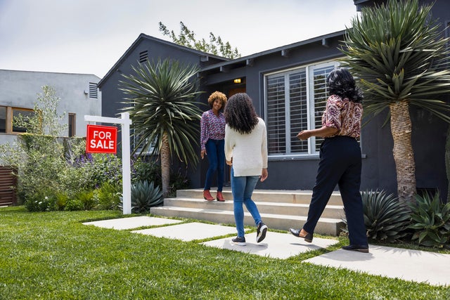 Full length of saleswoman greeting female customers while standing outside house 