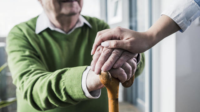 Close-up of woman holding senior man's hand leaning on cane 