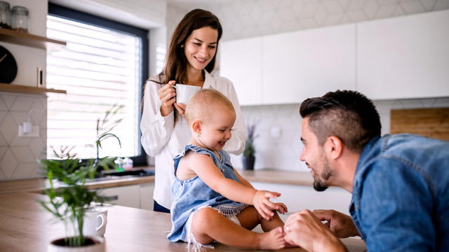 Portrait of young couple with toddler girl standing indoors in kitchen at home. 