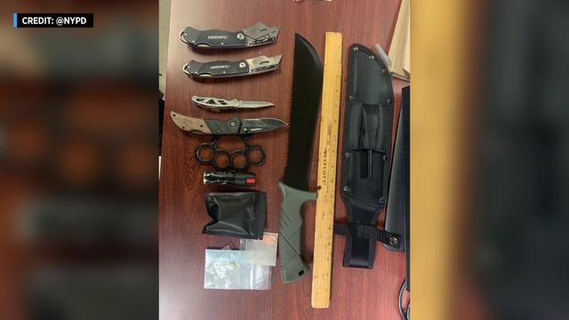 A photo of a large knife, two box cutters, two smaller knives, brass knuckles, pepper spray and pills in bags. 