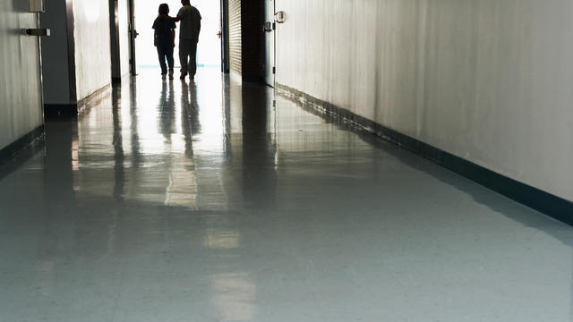 Two people standing at end of corridor in hospital 