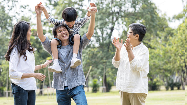 Multi Asian family spending time in weekend holiday. Young father carry kid piggyback in public park happy together. 