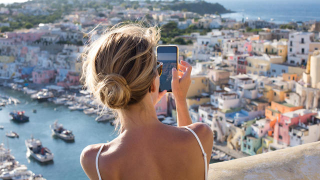 Woman taking pictures of the idyllic port of Corricella, Procida Island, Italy 