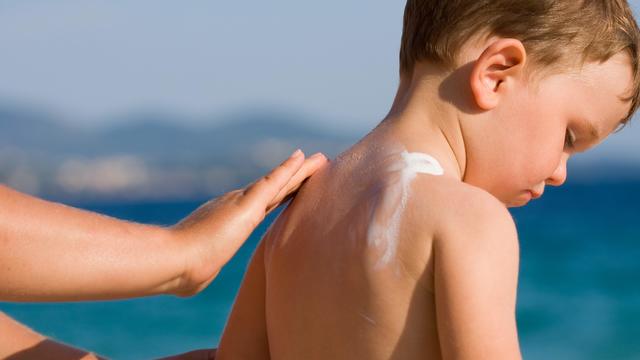Woman applying sunscreen on a child's back at the beach 