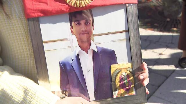 A woman holds a framed photo of Devesh Samtani. 