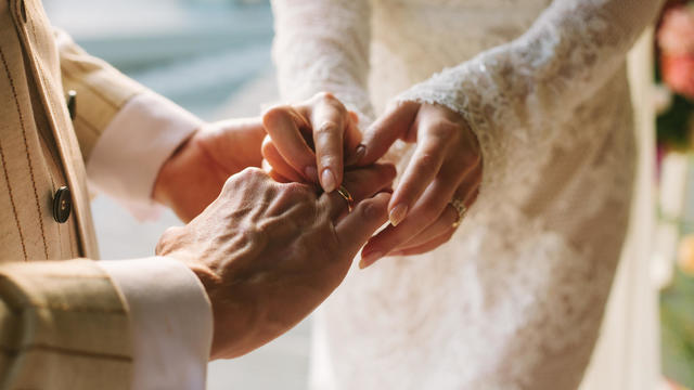 Bride putting ring on groom's finger. Rings exchange. Happy couple celebrating wedding outdoors in summer. 