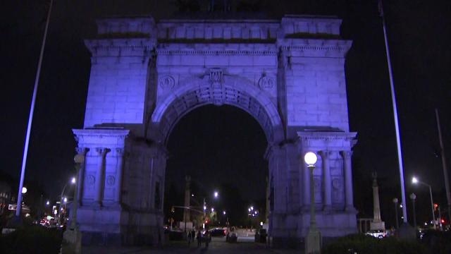 The Soldiers and Sailors Memorial Arch at Grand Army Plaza lit in purple at night. 