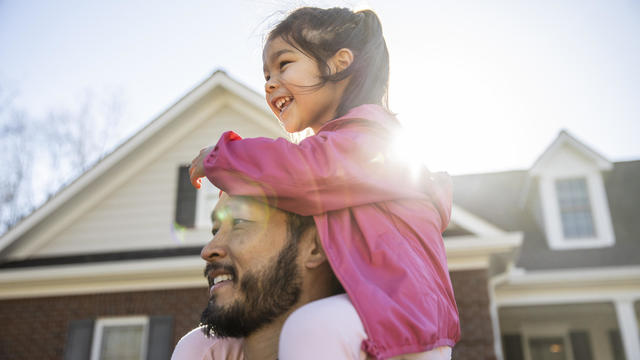 Daughter on father's shoulders in front of suburban home 