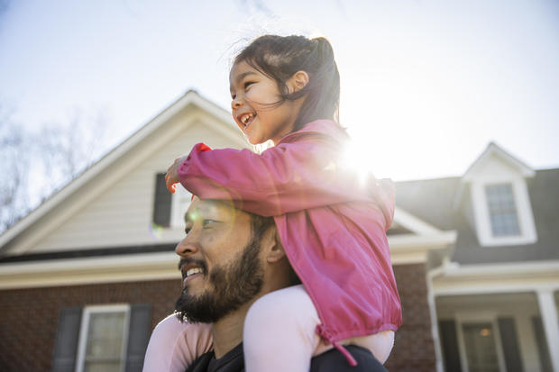 Daughter on father's shoulders in front of suburban house 