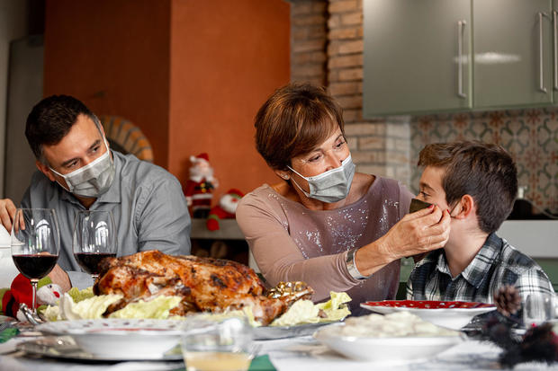 Grandmother adjust the surgical mask to her grandson during Christmas dinner. 