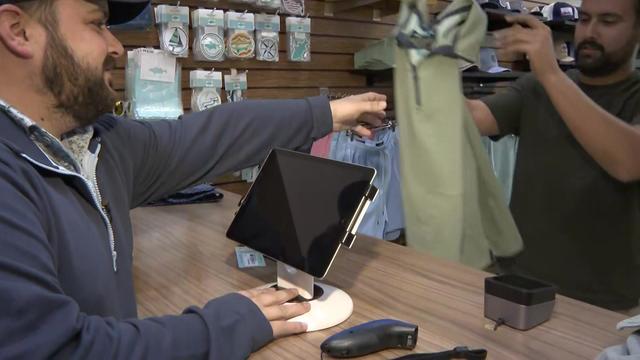 A customer hands a sweater to a store employee behind a counter. 