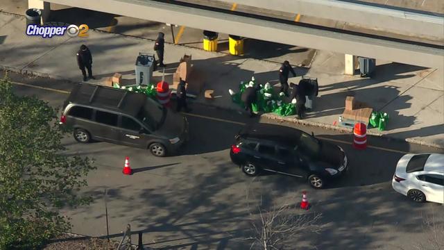 Cars wait in line while volunteers hand out bags of food. 