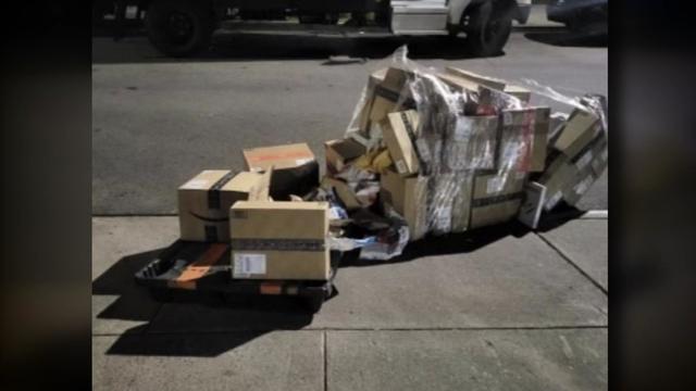 A pallet of Amazon packages lays on the sidewalk. Some packages have been opened and rummaged through. 