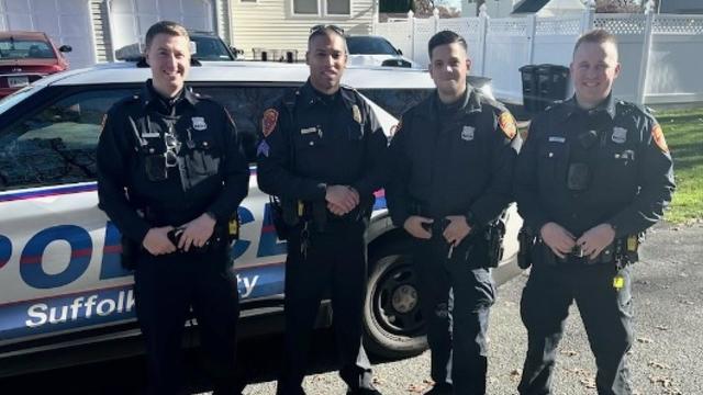 Four Suffolk County police officers pose in front of a Suffolk County police vehicle. 