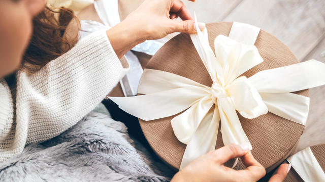 Close-up of a woman wrapping gifts and tying a beautiful pastel ribbon bow 